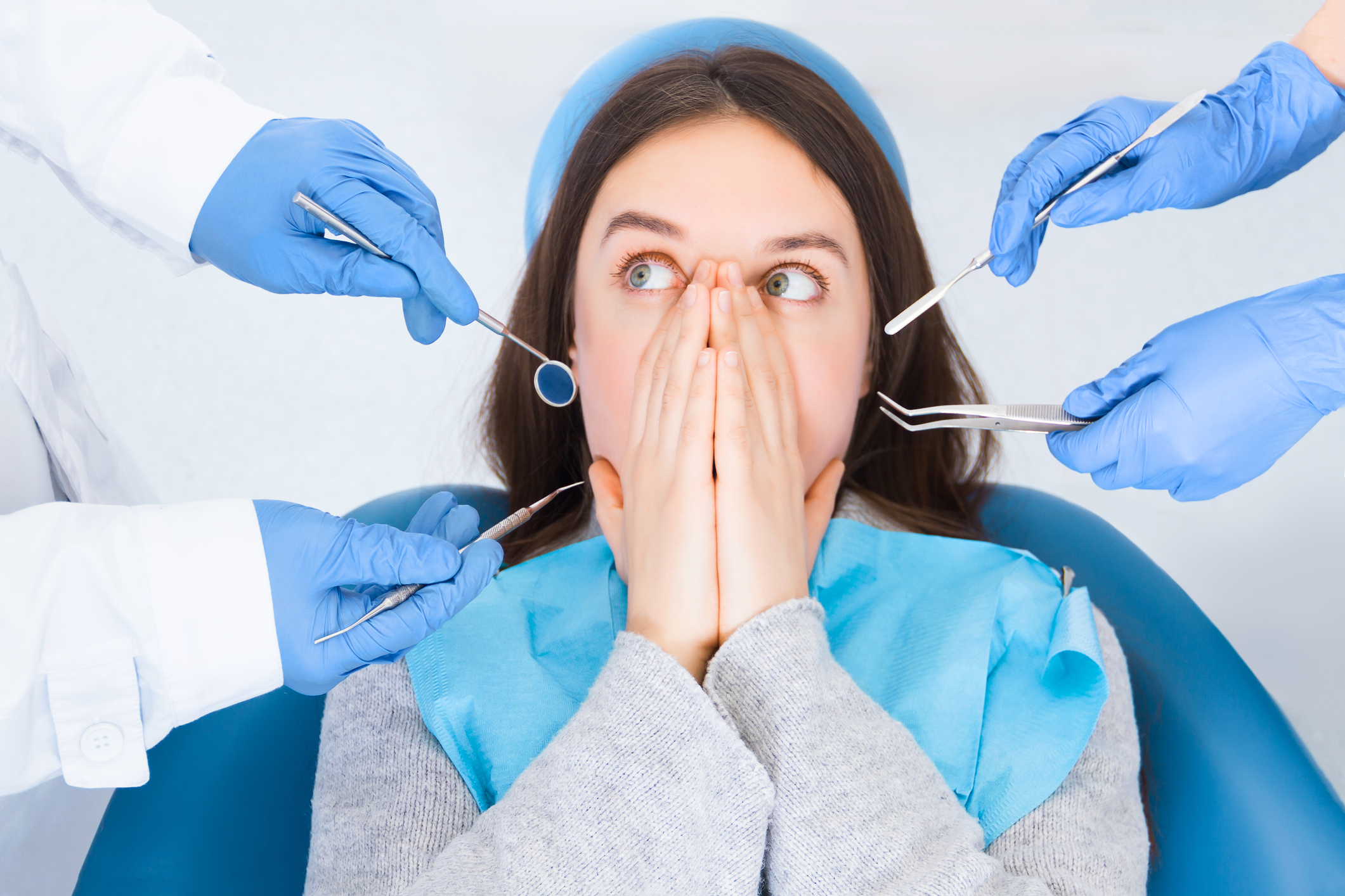 Closeup doctor hands in gloves are holding dental instruments in clinic, office. Scared woman is closing her mouth with hands, preventing examining of teeth, because of fear. Visiting dentist concept.