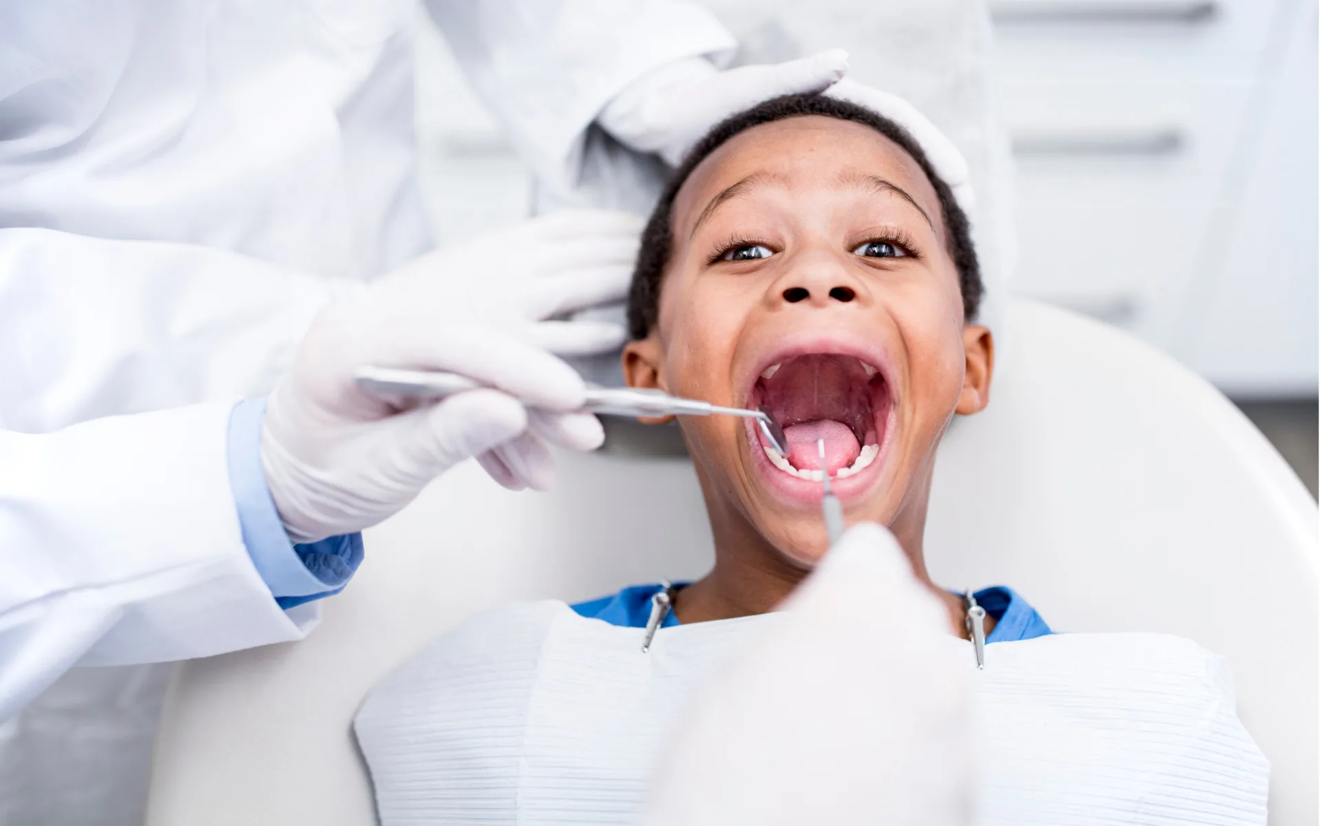 Enfant allongé au fauteuil, bouche ouverte, examiné au miroir par le dentiste ganté