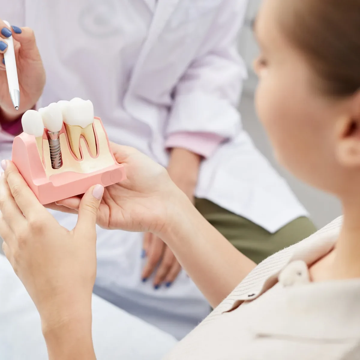 Implants et prothèses dentaires, un praticien présente une maquette d’implant à une patiente